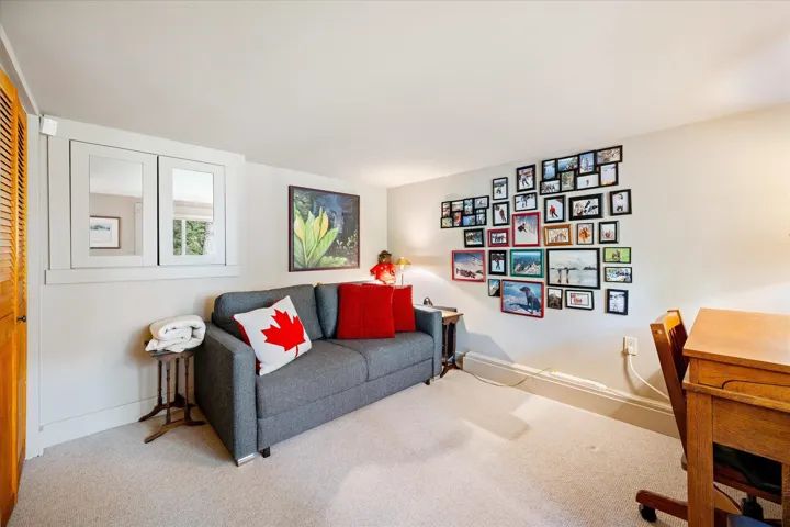 Carpeted room featuring a built-in window with white trim, light beige walls, and wood-finish louvered doors
