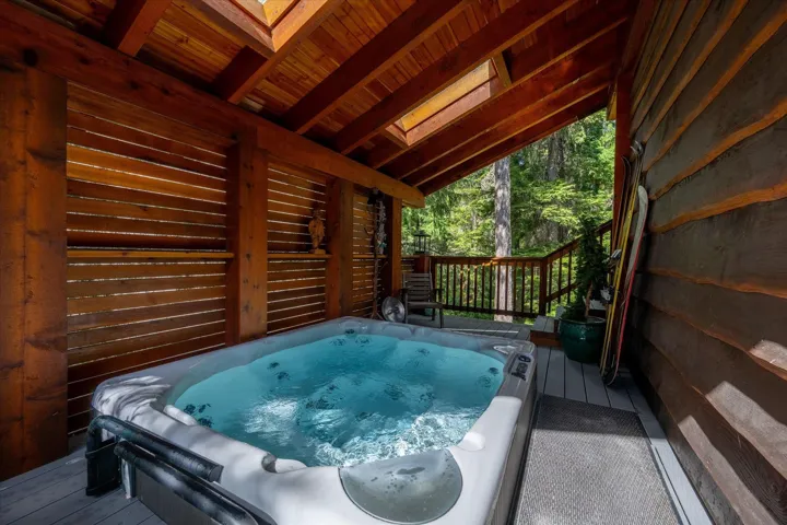 Covered outdoor spa area featuring a built-in hot tub, slatted wood privacy screen, exposed timber beams, and a skylight