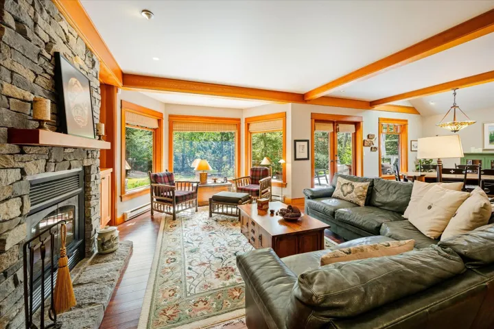 Spacious living area featuring a floor-to-ceiling stone fireplace with a wood mantel, exposed wood ceiling beams, and wood-finish flooring