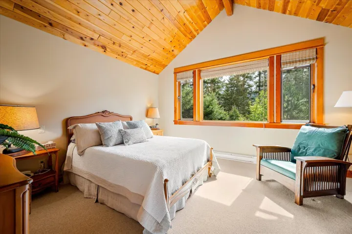 Bedroom featuring an angled wood-paneled ceiling, a large window with wood trim, and wall-to-wall carpeting