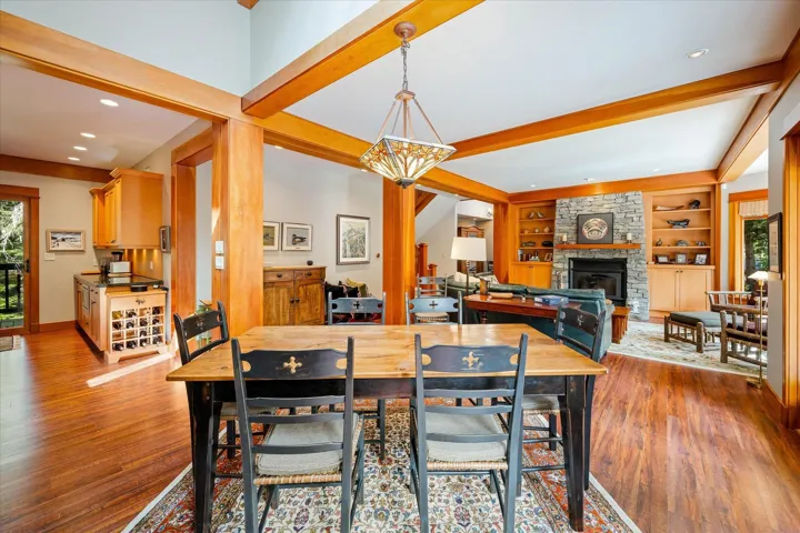 Open-concept dining and living areas featuring extensive wood-finish flooring, exposed wood beams, and recessed lighting