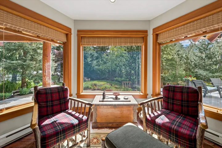 Corner window seating area featuring expansive windows with wood trim, woven blinds, and broad views of mature trees and landscaping