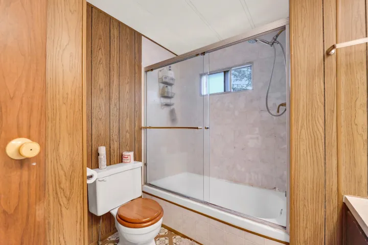 Bathroom with tiled shower / bath combo, vanity, and wood walls
