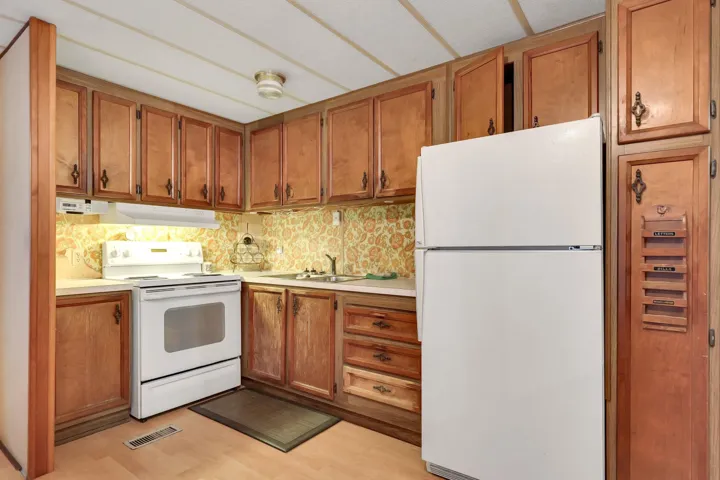 Kitchen featuring white appliances, light countertops, brown cabinetry, under cabinet range hood, and light wood-style flooring
