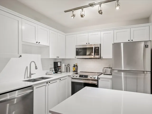 Kitchen with appliances with stainless steel finishes, white cabinets, decorative backsplash, and light stone counters