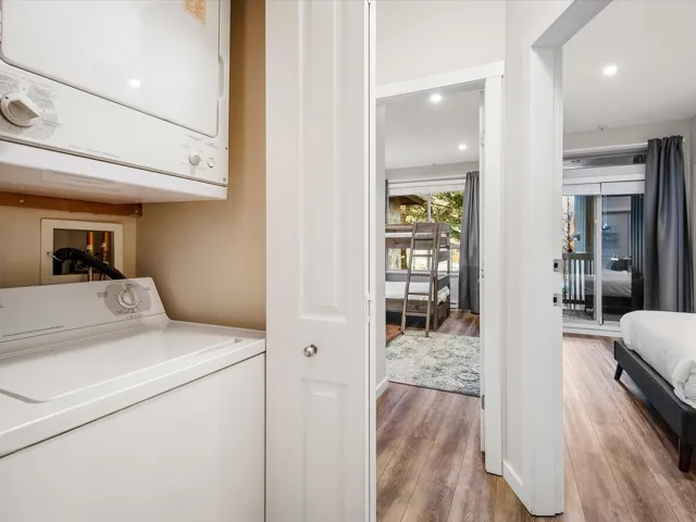 Laundry area with wood finished floors, stacked washer and clothes dryer, and recessed lighting