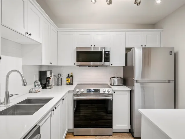 Kitchen with appliances with stainless steel finishes, white cabinets, tasteful backsplash, and light stone counters