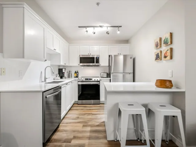 Kitchen featuring a breakfast bar, appliances with stainless steel finishes, white cabinets, light wood finished floors, and a peninsula