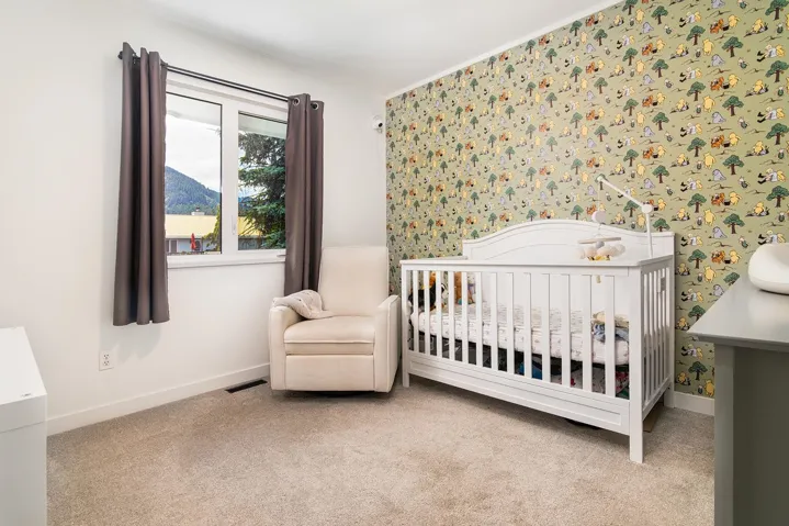 Carpeted bedroom with wallpapered walls, a nursery area, and crown molding