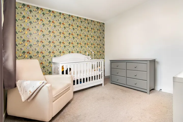 Carpeted bedroom with wallpapered walls, a nursery area, and ornamental molding
