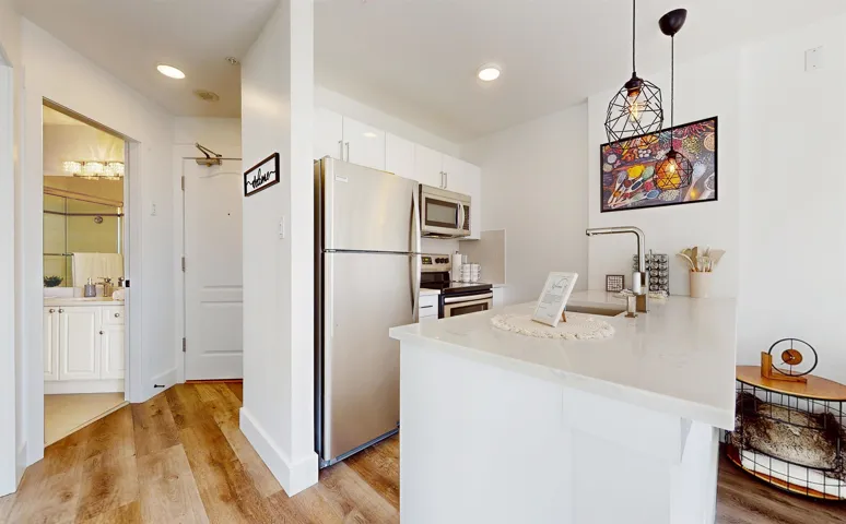 Kitchen with a peninsula, stainless steel appliances, white cabinetry, pendant lighting, and light wood finished floors