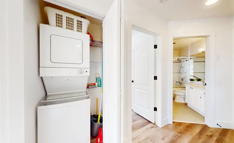 Laundry area with stacked washer / drying machine and light wood-type flooring