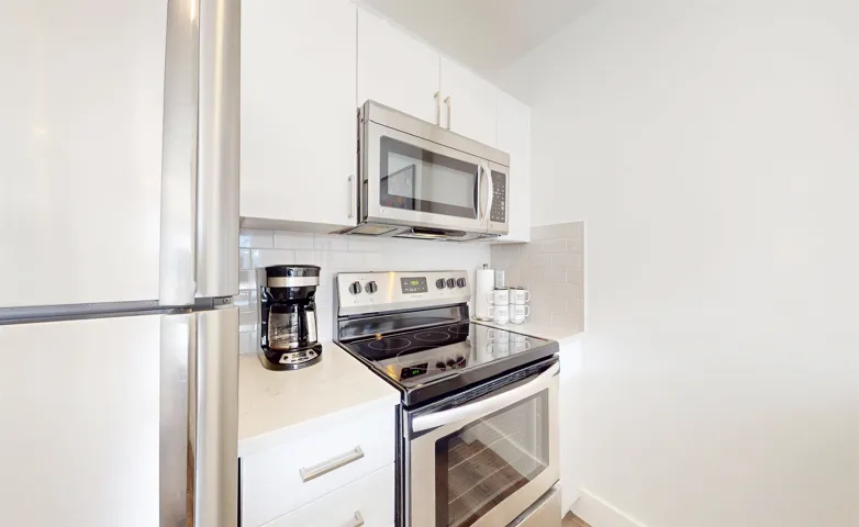 Kitchen featuring stainless steel appliances, white cabinets, and light stone countertops
