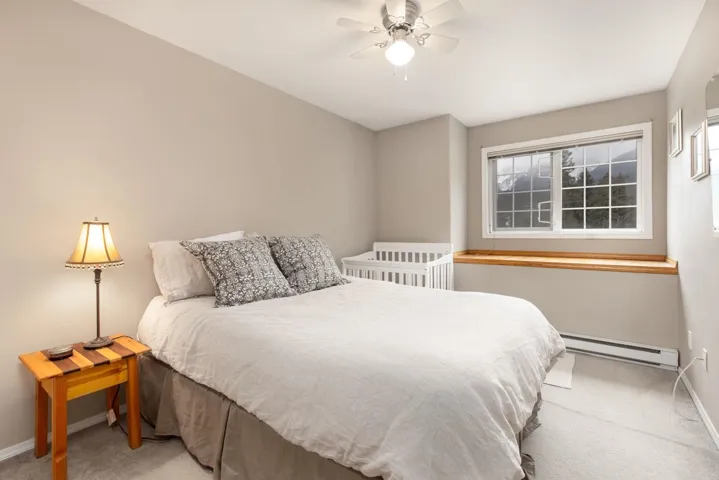 Carpeted bedroom with baseboards, a ceiling fan, baseboard heating, and multiple windows