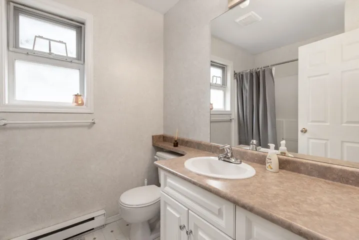 Bathroom featuring visible vents, toilet, vanity, a shower with shower curtain, and baseboard heating