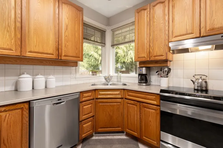 Kitchen featuring decorative backsplash, stainless steel appliances, under cabinet range hood, and a sink