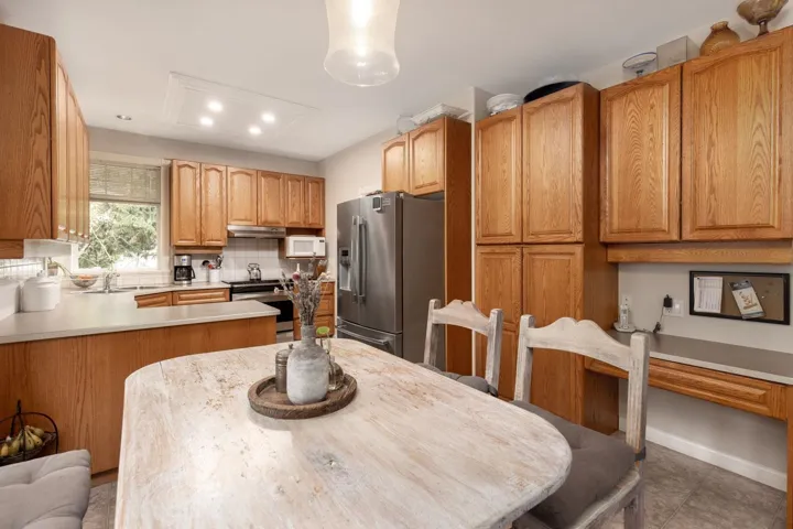 Kitchen with tile patterned flooring, under cabinet range hood, stainless steel appliances, light countertops, and decorative backsplash