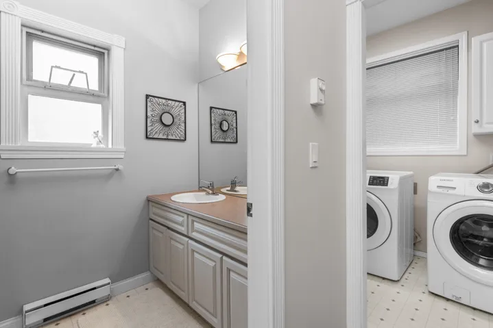 Washroom with a baseboard heating unit, a sink, washing machine and dryer, light floors, and laundry area