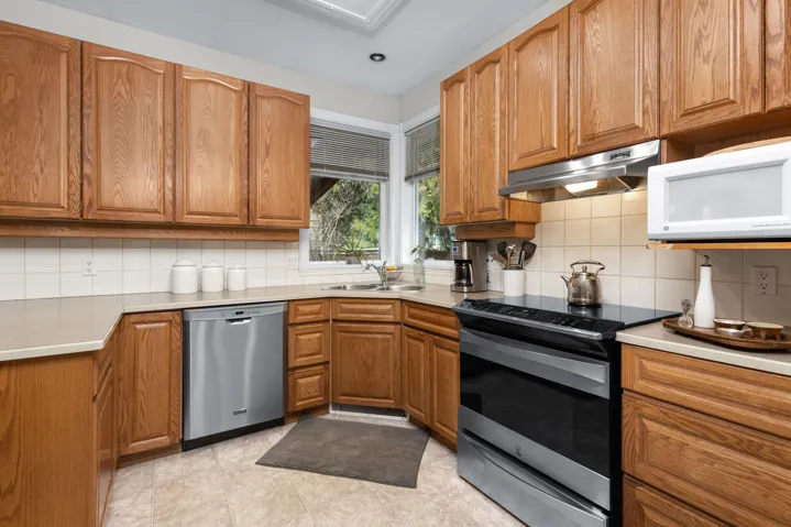 Kitchen featuring brown cabinetry, under cabinet range hood, and stainless steel appliances