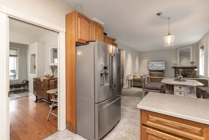 Kitchen with light wood-type flooring, open floor plan, stainless steel fridge with ice dispenser, light countertops, and hanging light fixtures