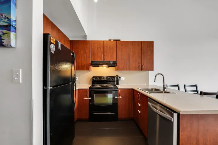 Kitchen with a peninsula, black appliances, a kitchen bar, light countertops, and dark tile patterned flooring