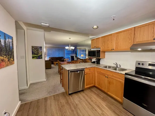 Kitchen featuring under cabinet range hood, open floor plan, appliances with stainless steel finishes, a peninsula, and a sink