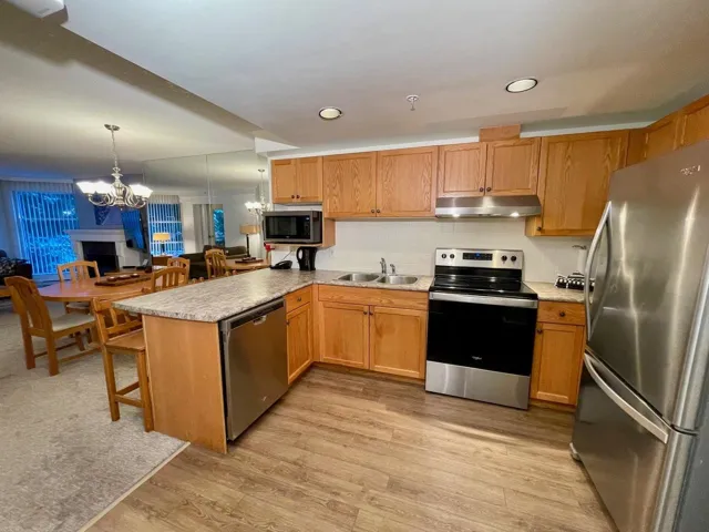 Kitchen with under cabinet range hood, a chandelier, a peninsula, stainless steel appliances, and a sink