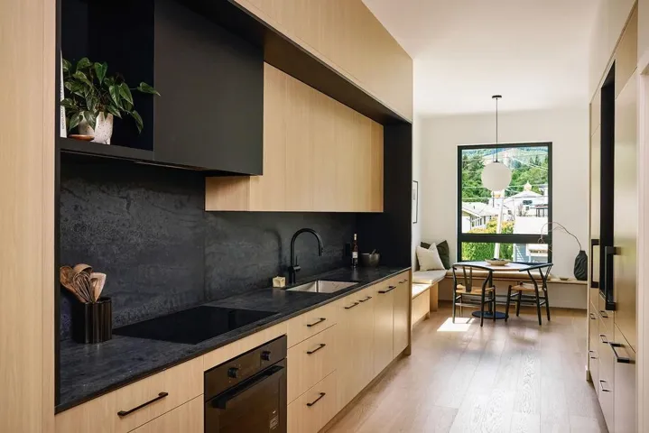 Contemporary kitchen featuring blonde wood-finish cabinetry, dark stone countertops, and integrated appliances