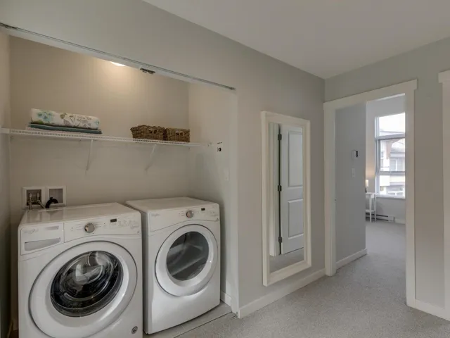 Laundry area with washing machine and dryer, light colored carpet, and baseboard heating