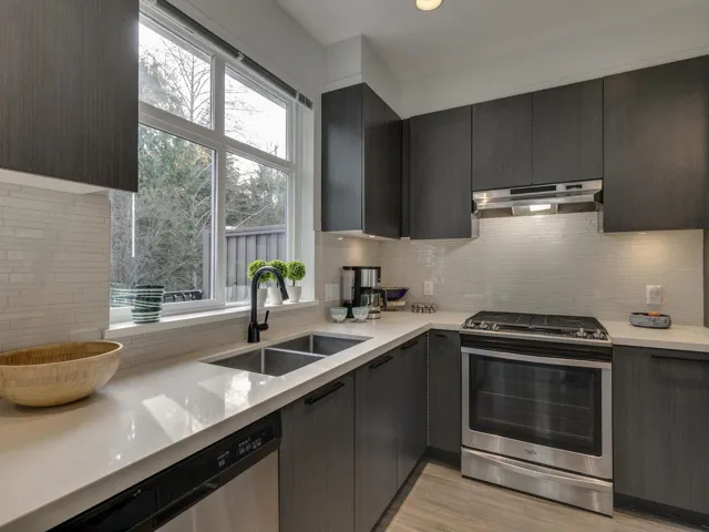 Kitchen with appliances with stainless steel finishes, backsplash, modern cabinets, under cabinet range hood, and light stone countertops