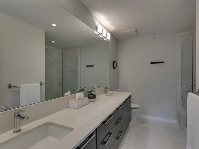 Bathroom featuring a textured ceiling, double vanity, and a shower stall