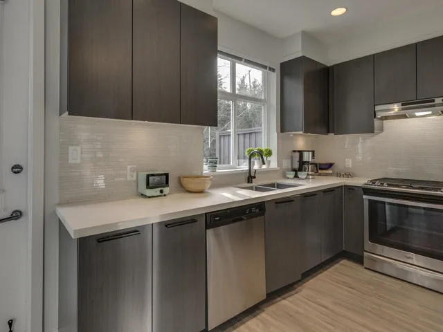 Kitchen featuring stainless steel appliances, modern cabinets, under cabinet range hood, tasteful backsplash, and light wood-style flooring