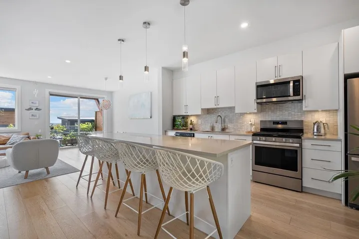 Kitchen with stainless steel appliances, light wood-style flooring, tasteful backsplash, a breakfast bar, and a kitchen island
