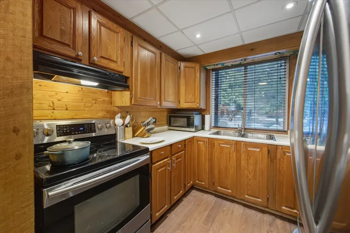 Kitchen featuring stainless steel appliances, brown cabinets, under cabinet range hood, light countertops, and recessed lighting