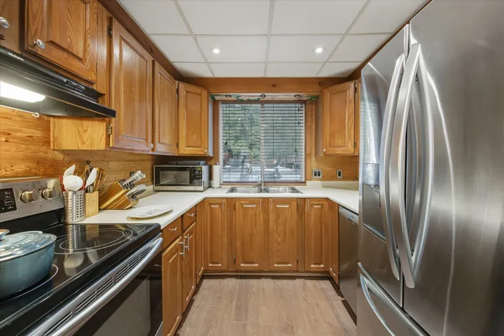 Kitchen featuring stainless steel appliances, brown cabinetry, light countertops, ventilation hood, and light wood-style flooring