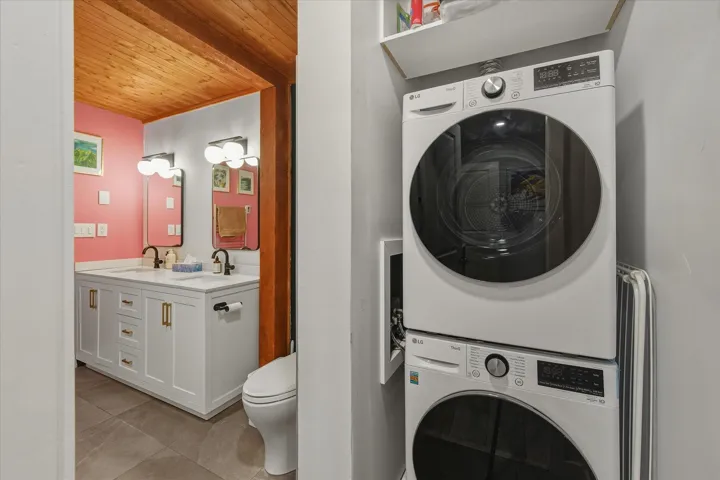 Full bath featuring double vanity, wood ceiling, stacked washer / dryer, and light tile patterned floors