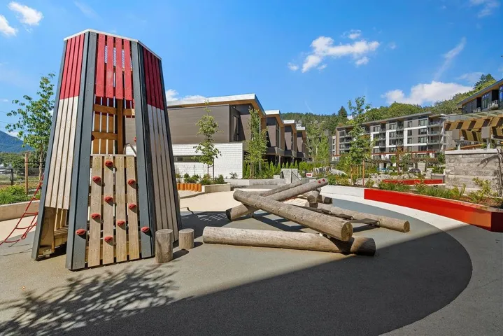 Outdoor play area featuring a multi-colored wood play structure, climbing holds, and natural wood log elements
