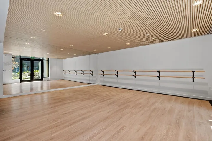 Spacious studio featuring wood-finish flooring, full-wall mirrors, and a slatted wood-panel ceiling with recessed lighting