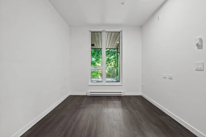 Bright room featuring a large window, dark wood-finish flooring, white walls, and white baseboards