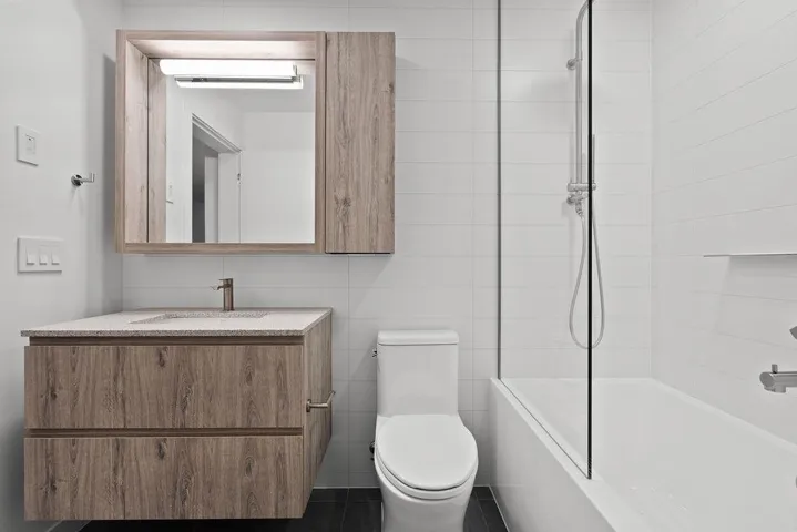 Modern bathroom featuring a floating wood-finish vanity with an integrated sink, coordinating medicine cabinet, full-size tub with glass partition, and white subway tile surround