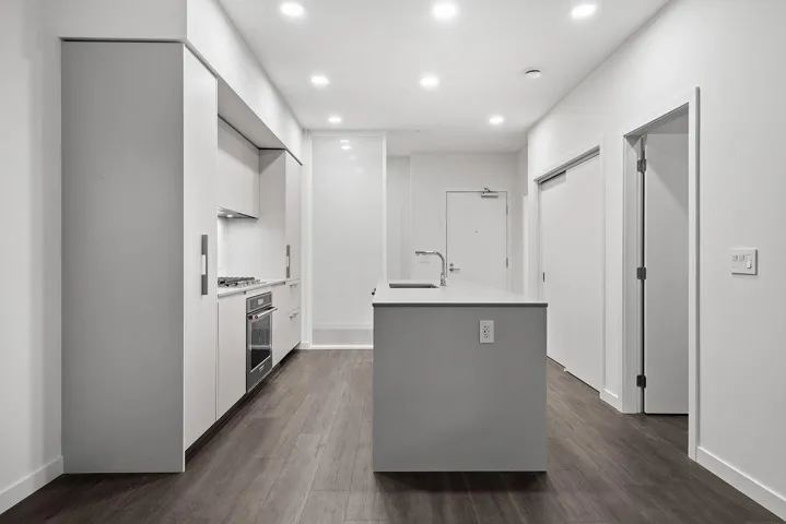 Modern kitchen featuring an island with integrated sink, stainless steel appliances, flush cabinetry, recessed lighting, and wood-finish flooring