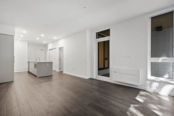 Open-concept living area featuring wood-finish flooring, recessed lighting, a kitchen island with an integrated sink, and an exterior door with accompanying window