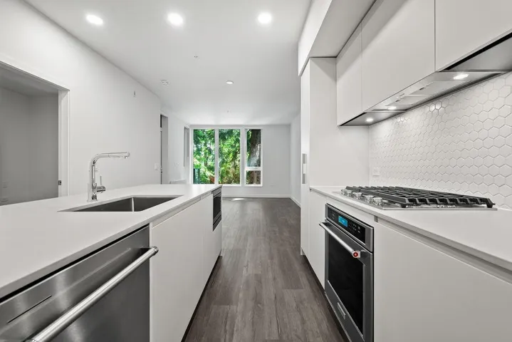 Modern kitchen featuring white flat-panel cabinetry, a hexagon tile backsplash, and stainless steel appliances