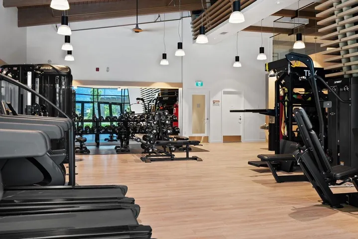 Fitness center featuring light wood-finish flooring, high ceilings with exposed beams, pendant lighting, and an extensive selection of exercise equipment