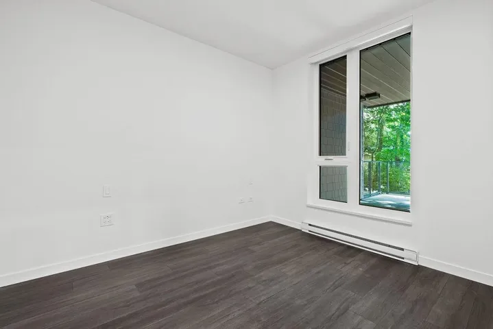 Bright interior space featuring a large white-framed window, dark wood-finish flooring, white baseboards, and a baseboard heater