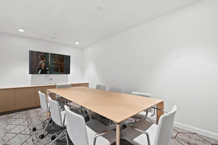 Conference room with a large flat-screen display, built-in wood-finish cabinetry, recessed lighting, and patterned carpet flooring