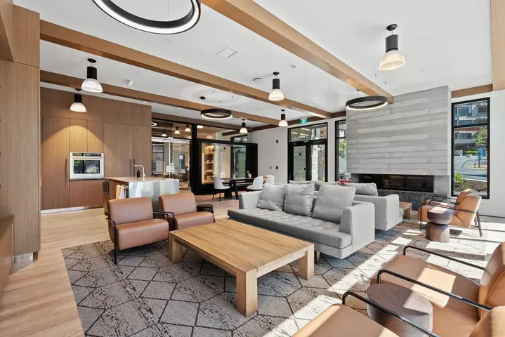 Open concept gathering area featuring wood-finish flooring, a linear fireplace set into a textured stone wall, and a built-in kitchen area with stainless steel appliances
