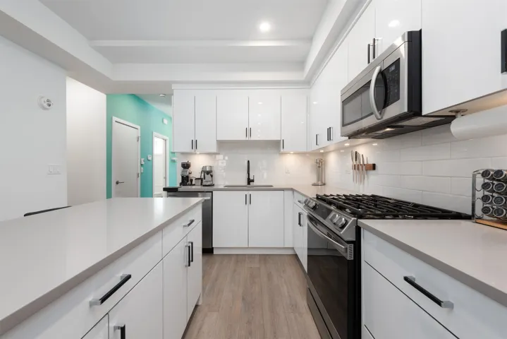Kitchen featuring appliances with stainless steel finishes, white cabinetry, light wood-style floors, light countertops, and decorative backsplash