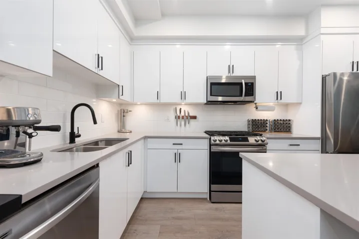 Kitchen with appliances with stainless steel finishes, white cabinets, tasteful backsplash, and light countertops