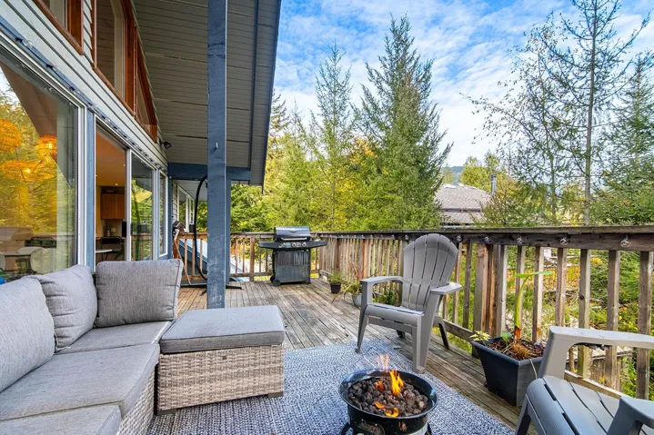 Wooden terrace featuring grilling area, an outdoor living space with a fire pit, and view of wooded area